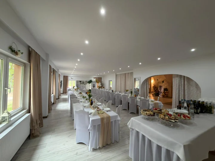 Sala z długimi stołami i łukowym przejściem — panorama wnętrza